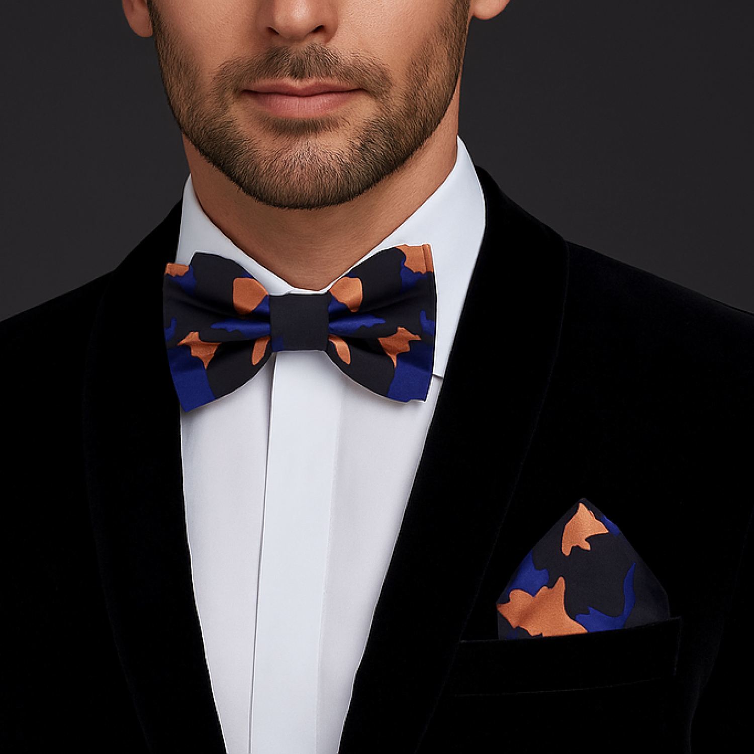Man wearing a black suit with a patterned blue, orange and black camo bow tie and pocket square on a dark background