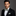 Man wearing a black suit with a green bow tie and pocket square on a gray background