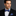 Man wearing a black suit with a blue bow tie and pocket square on a gray background