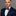 Man wearing a navy suit with a patterned bow tie and pocket square on a gray background