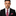 Man wearing a black suit with a red, white, and blue striped tie and pocket square on a white background