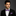 Man wearing a black suit with a purple bow tie and matching pocket square on a gray background