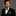 Man wearing a black suit with a green bow tie and pocket square on a gray background