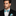 Man wearing a black suit with a blue bow tie and pocket square against a gray background
