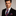 Man wearing a suit with a blue, red and white plaid tie and pocket square on a plain background