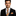Man wearing a black suit with an orange plaid tie and pocket square on a white background