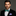 Man wearing a black suit with a green bow tie and purple pocket square on a gray background