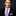 Man wearing a black suit with a purple and gray striped tie and matching pocket square on a dark background