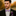 Man in a suit with a purple bow tie and boutonniere against a blurred natural background