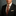 Man wearing a black suit with a patterned tie against a gray background