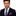 Man wearing a dark suit with a purple tie and pocket square on a white background