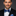 Man wearing a black suit with a blue bow tie and pocket square on a dark background