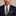 Man wearing a navy suit with a patterned tie and pocket square on a beige background