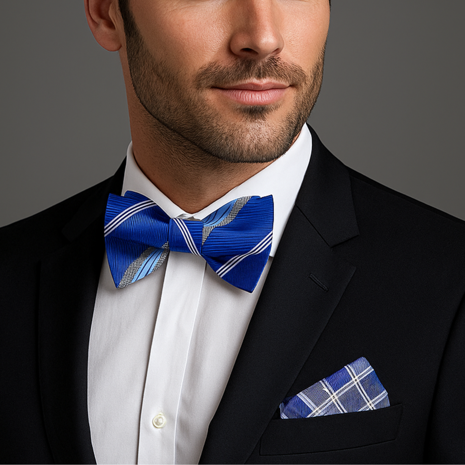 Man wearing a black suit with a blue bow tie and pocket square on a gray background