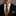Man wearing a black suit with a yellow and black checkered tie and pocket square against a gray background