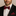 Man wearing a black suit with a red and black checkered bow tie and pocket square.