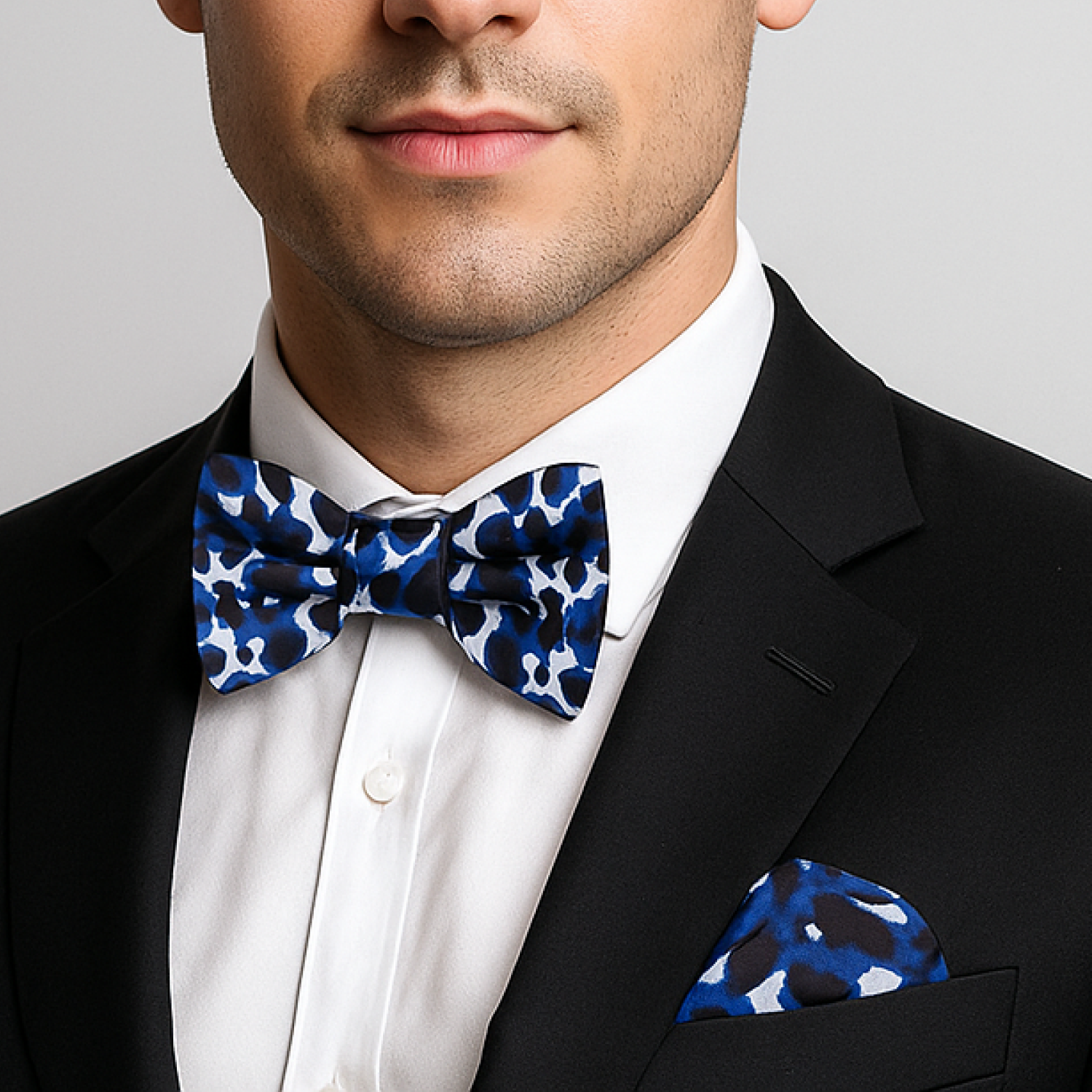 Man wearing a black suit with a white shirt and blue patterned bow tie and pocket square.