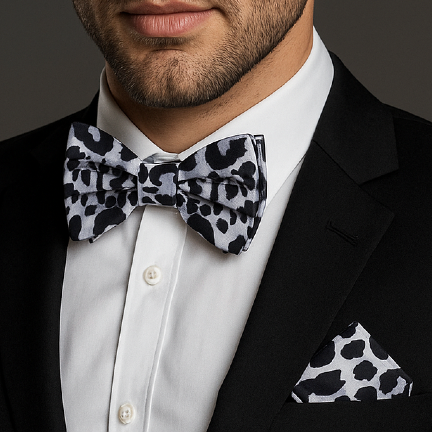 Man wearing a black and white patterned bow tie and pocket square with a dark background