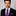 Man wearing a black suit with a purple plaid tie and pocket square on a gray background