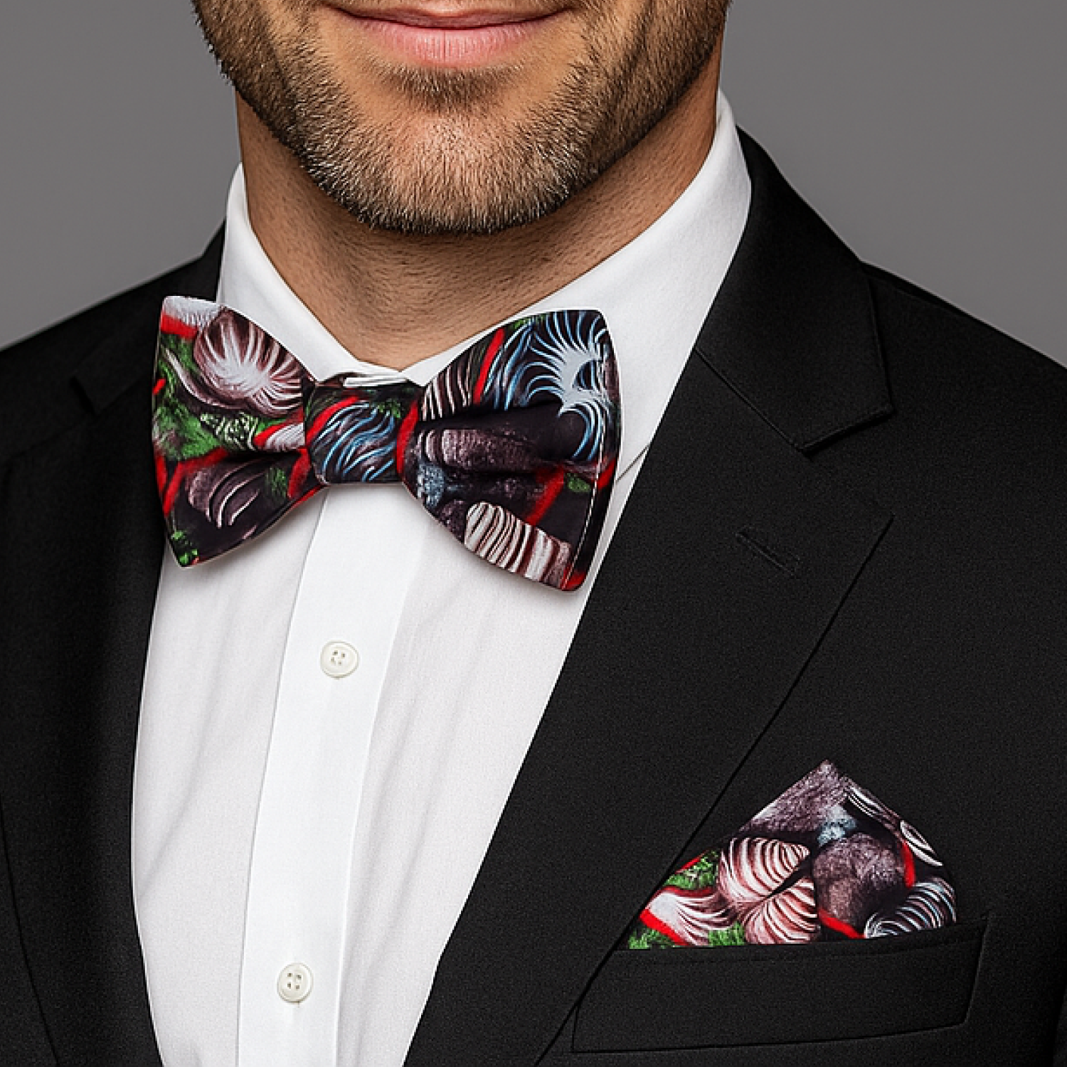 Man wearing a black suit with a colorful bow tie and pocket square against a gray background