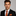 Man wearing a black suit with an orange tie and pocket square on a gray background