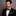 Man wearing a black tuxedo with a white shirt and polka dot bow tie and pocket square on a gray background