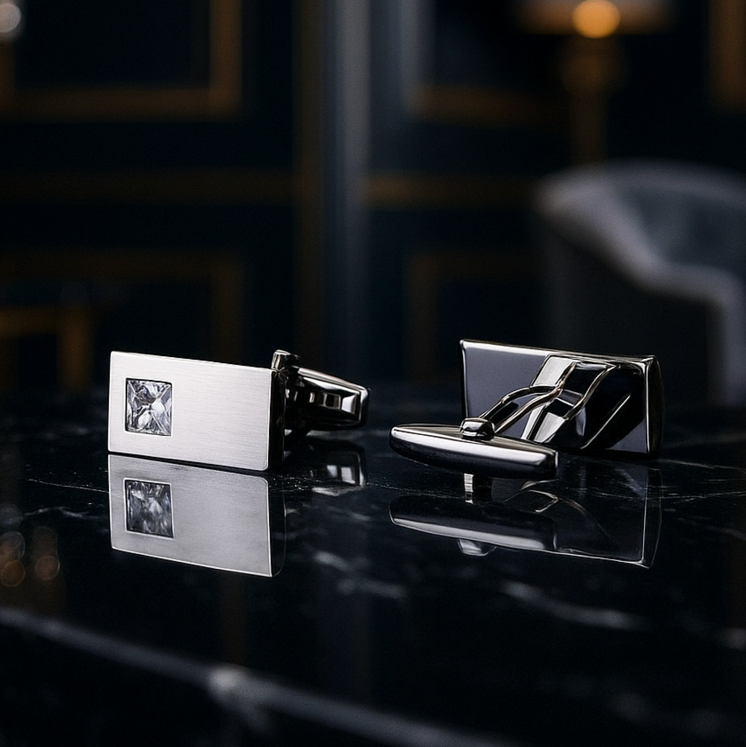 Pair of silver cufflinks on a reflective surface with a blurred background