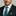 Man wearing a dark suit with a white shirt and teal patterned tie against a neutral background