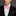 Man wearing a black suit with a white shirt and pink bow tie, against a dark background.
