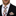 Man wearing a black suit with a plaid tie and pocket square on a white background