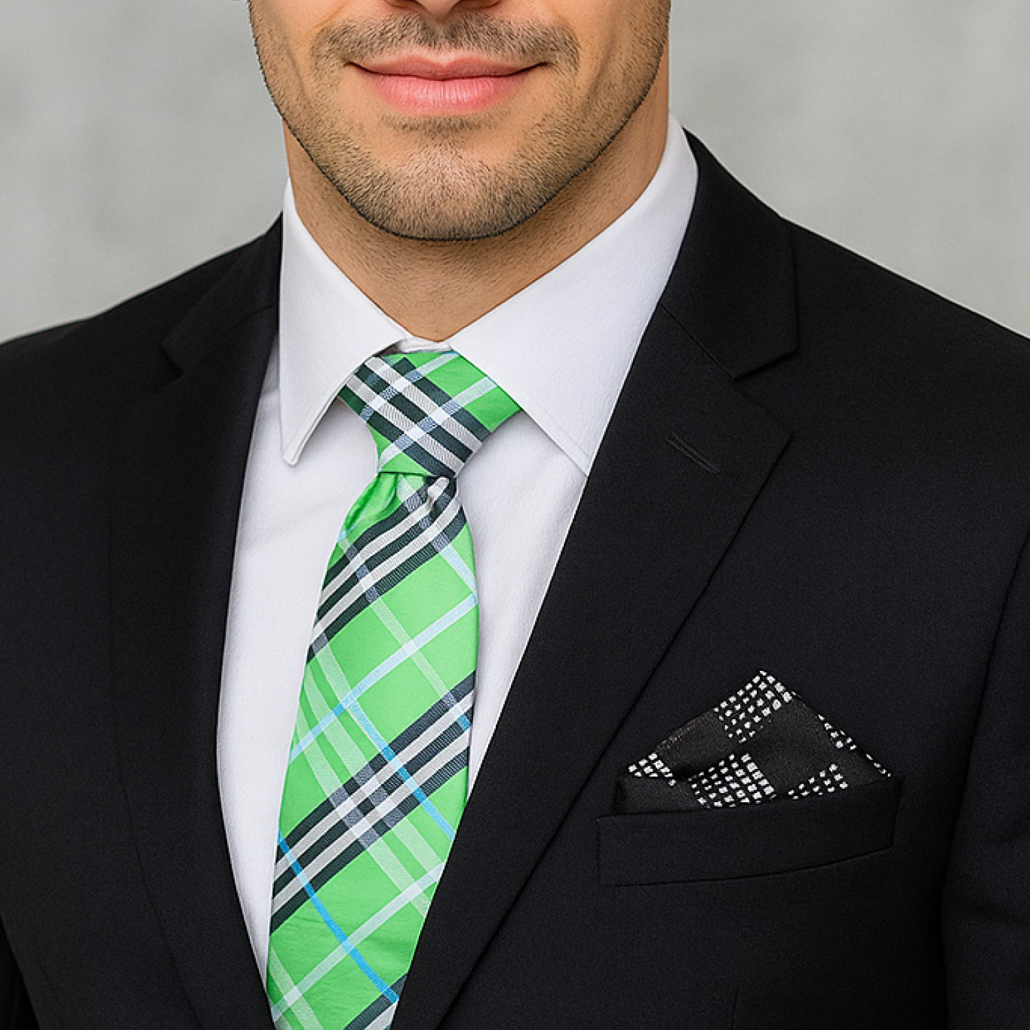 Man wearing a black suit with a green plaid tie and black pocket square against a gray background
