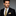 Man wearing a black suit with a gold tie and pocket square against a gray background