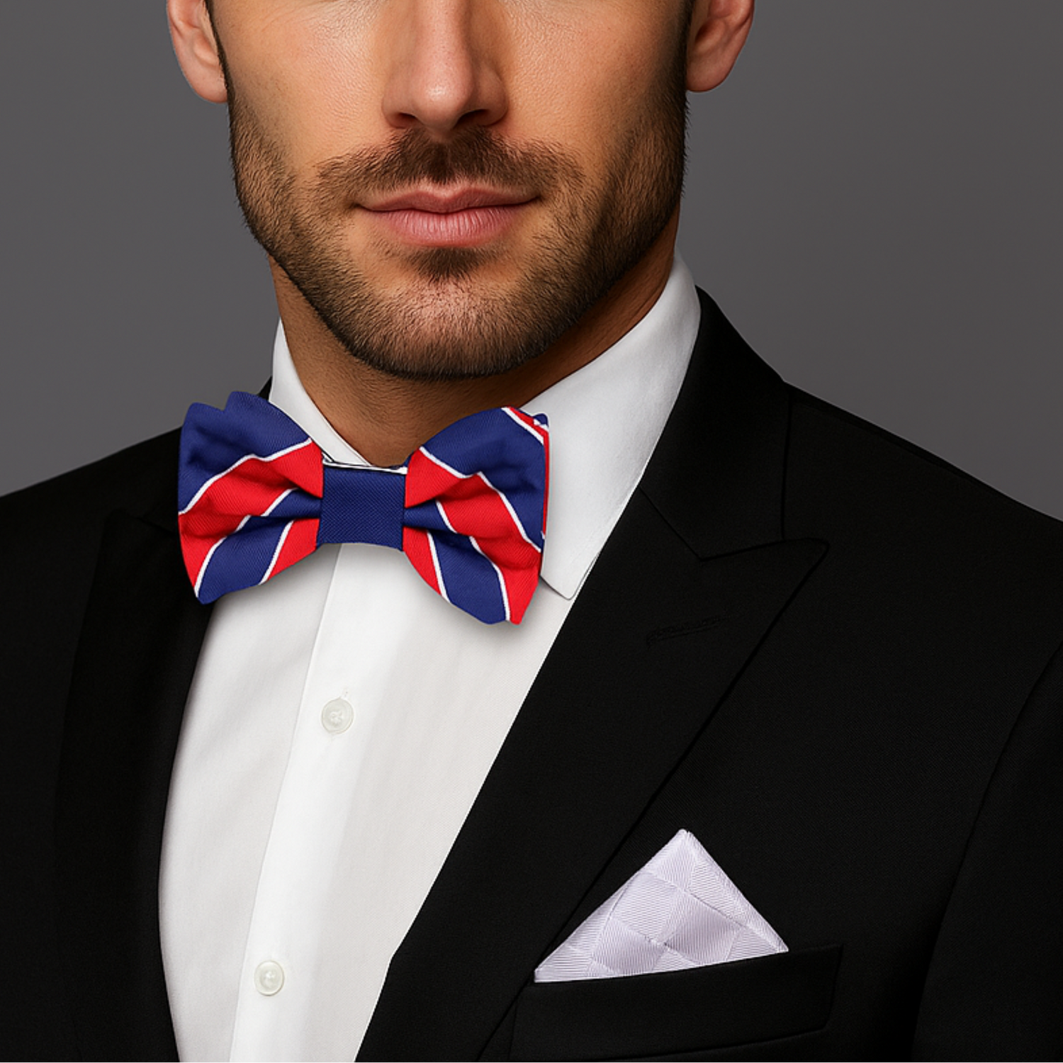 Man wearing a black suit with a white shirt and a red, blue, and white bow tie on a gray background