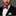 Man wearing a black suit with a white shirt and a red, blue, and white bow tie on a gray background