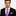 Man wearing a black suit with a purple checkered tie and pocket square on a white background