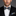 Man wearing a black suit with a blue and yellow geometric patterned bow tie and pocket square on a gray background