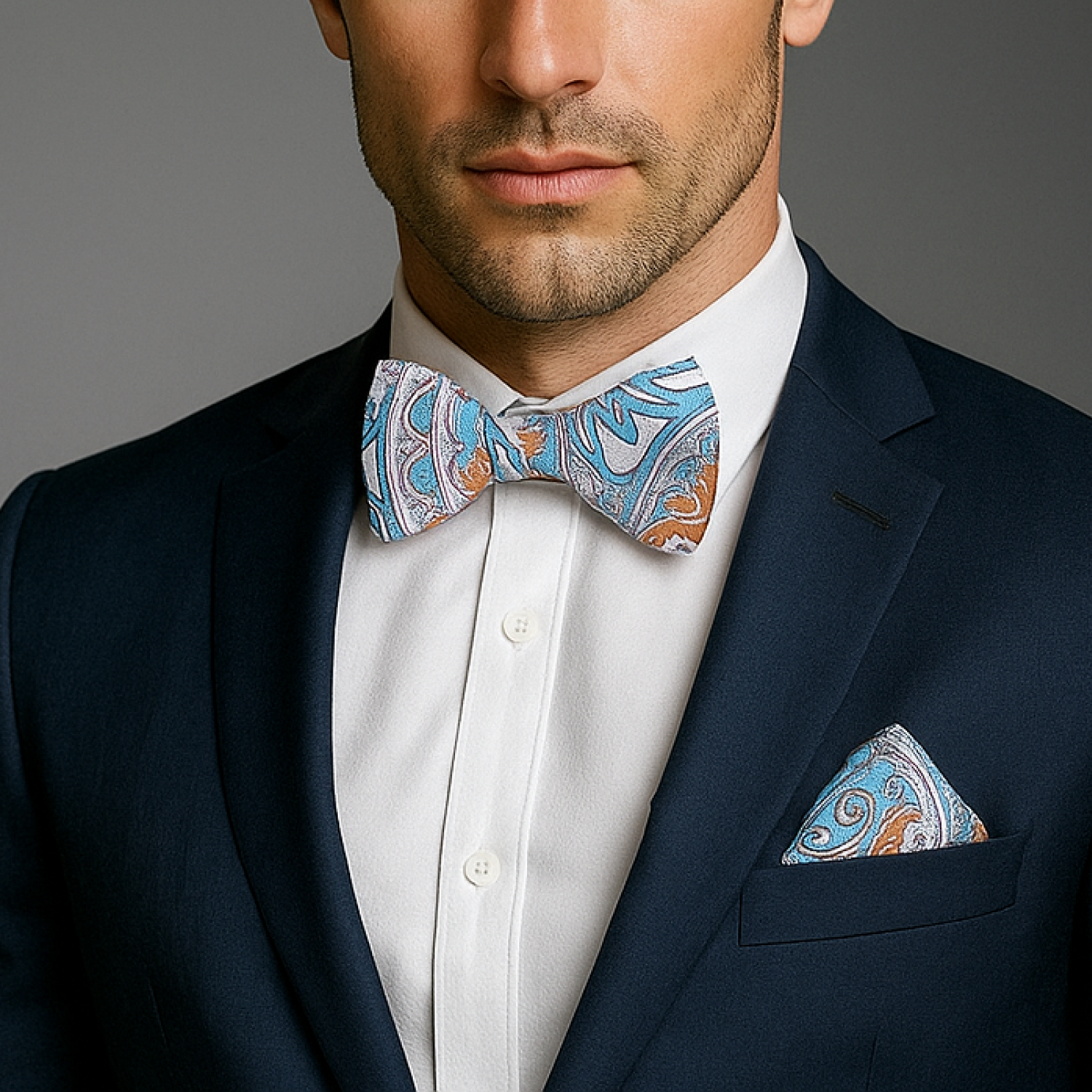 Man wearing a navy suit with a patterned bow tie and pocket square against a gray background