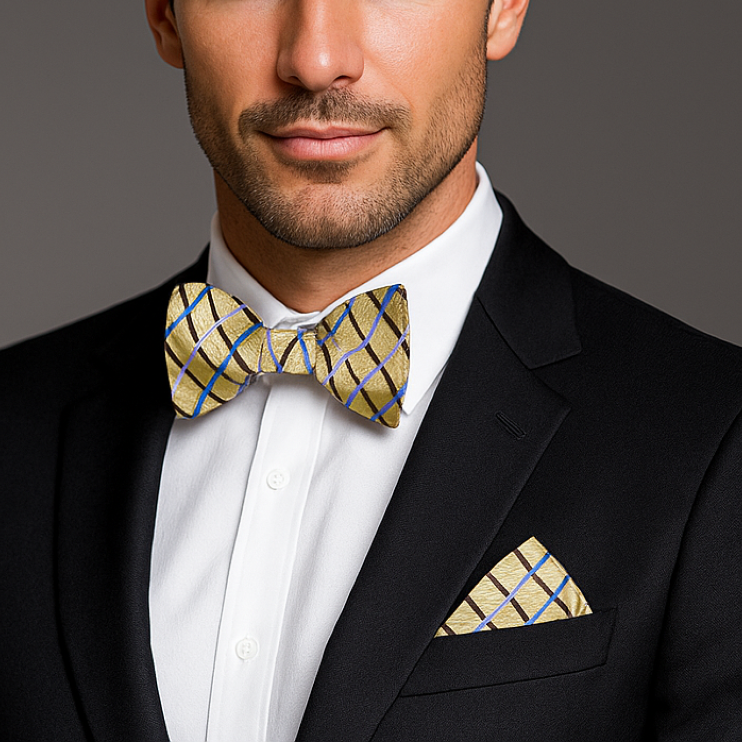 Man wearing a black suit with a white shirt, gold bow tie, and matching pocket square against a gray background.