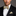 Man wearing a black suit with a white shirt, gold bow tie, and matching pocket square against a gray background.