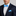 Man wearing a navy suit with a white shirt, blue patterned bow tie, and pocket square against a gray background.