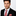 Man wearing a black suit with a red and white striped tie and pocket square on a light gray background