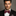 Man wearing a black suit with a red bow tie against a gray background