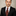 Man wearing a black suit with a patterned tie against a neutral background