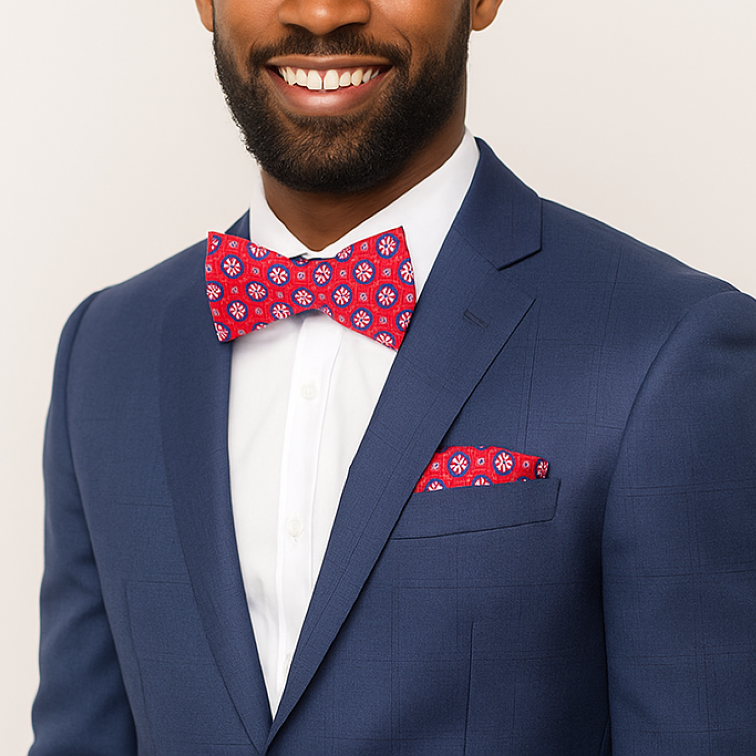 Man wearing a blue suit with a red patterned bow tie and pocket square on a plain background