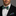 Man wearing a black suit with a green and purple checkered bow tie and pocket square.
