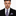 Man wearing a black suit with a red and blue patterned tie and pocket square on a white background