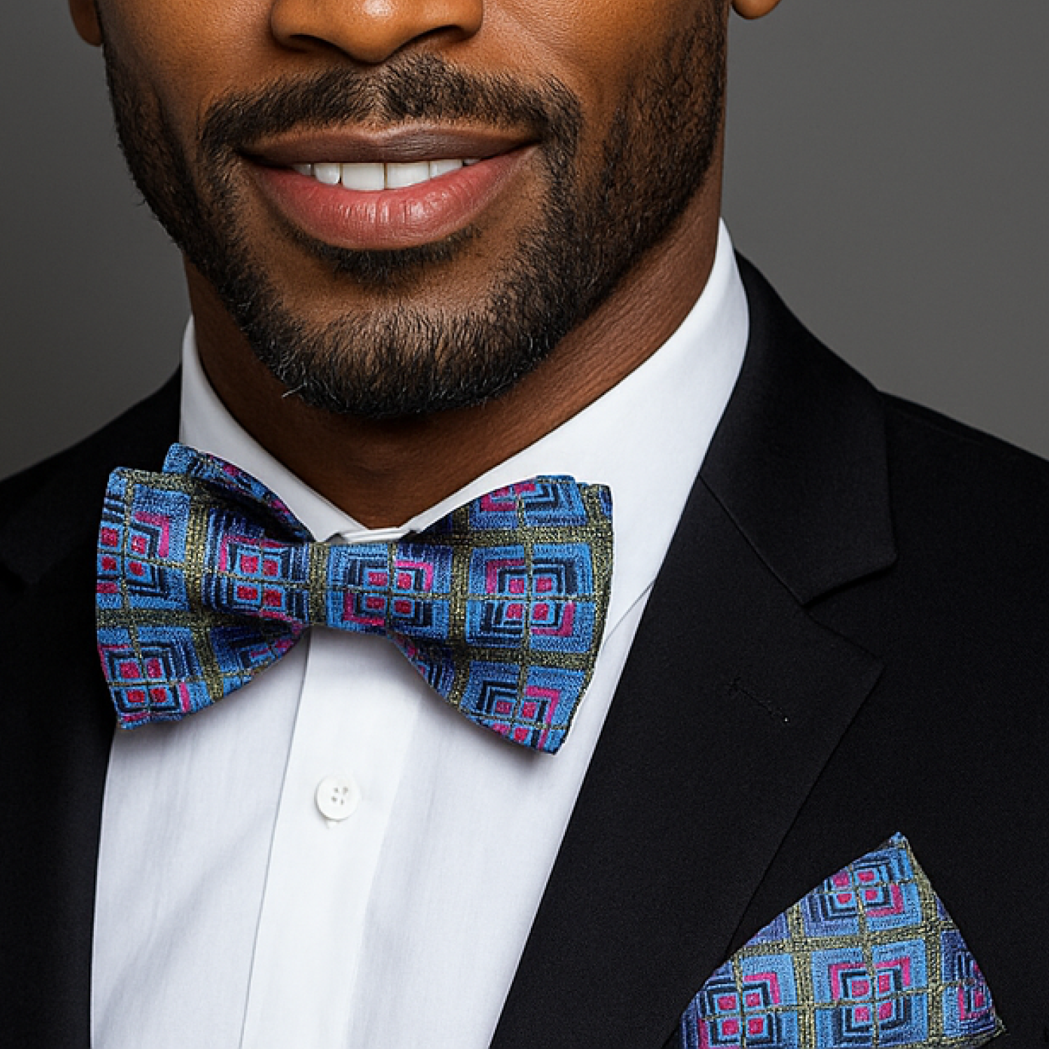 Man wearing a black suit with a colorful bow tie and pocket square against a gray background