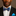 Man wearing a black suit with a white shirt, blue bow tie, and blue pocket square against a brown background
