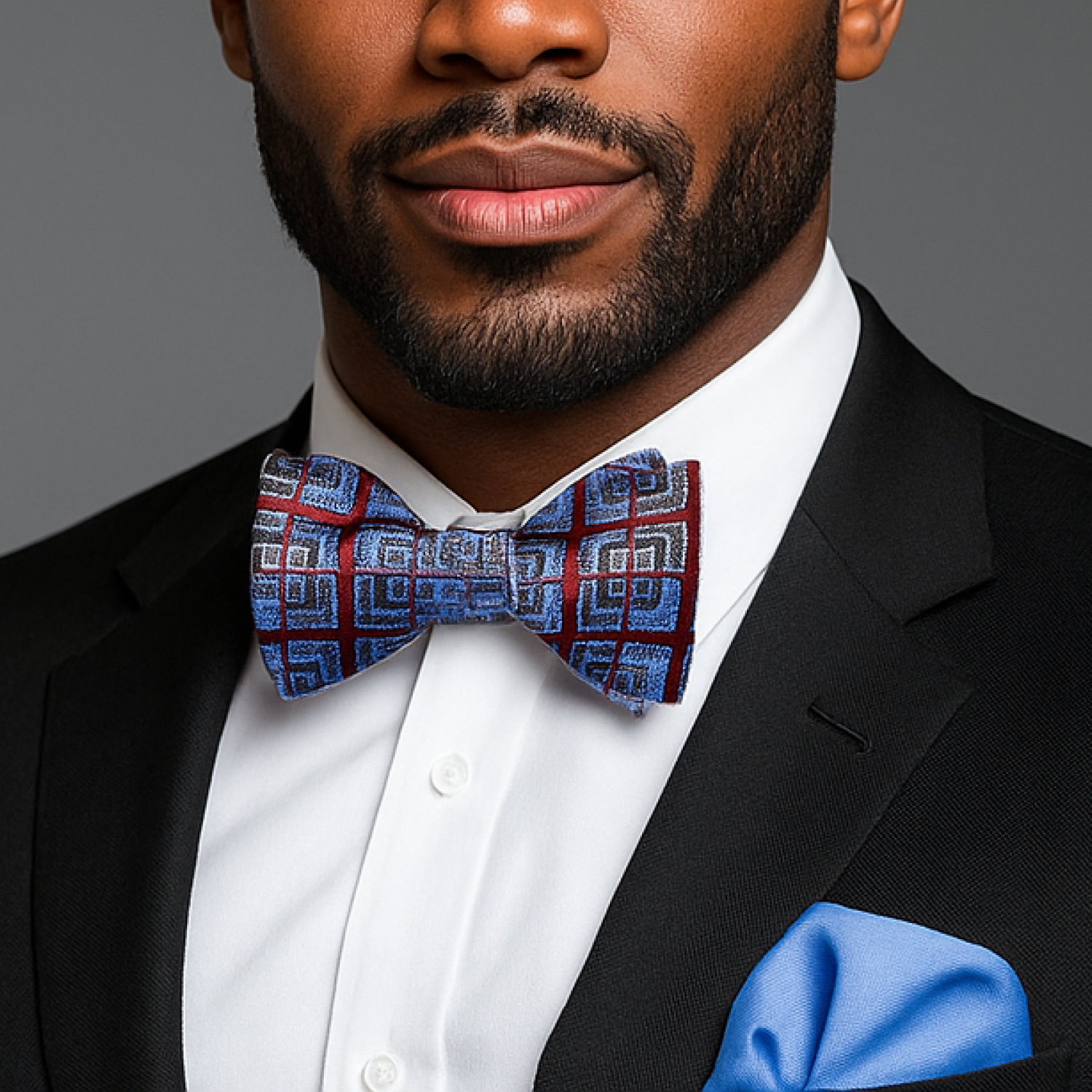 Man wearing a black suit with a blue and red patterned bow tie against a gray background