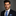 Man wearing a dark suit with a blue tie and pocket square against a gray background